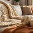 Close-up of a cozy crochet blanket made with super bulky yarn on a couch, with a crochet hook and yarn skeins beside it.