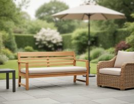 Outdoor patio furniture set with a teak bench, aluminum side table, and wicker lounge chair with neutral cushions in soft natural daylight.